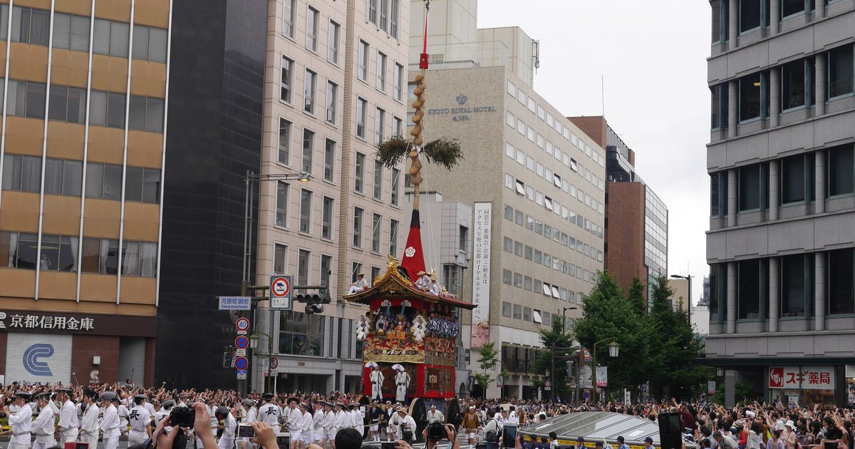 祇園祭前祭山鉾巡行:一座頂著長真木的鉾車行進在京都河原町通,路旁人群高舉手機拍攝