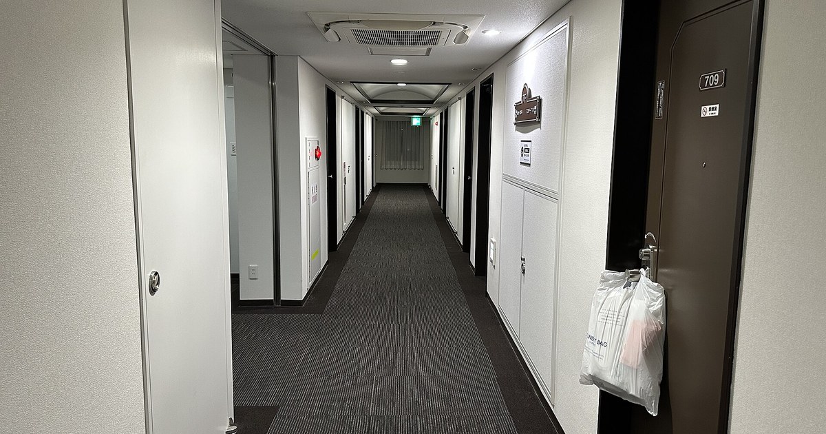 日本商務飯店的客房走廊,白牆配深褐色房門,709 號房門上掛著送洗衣物袋,走道盡頭是拉上窗簾的採光窗