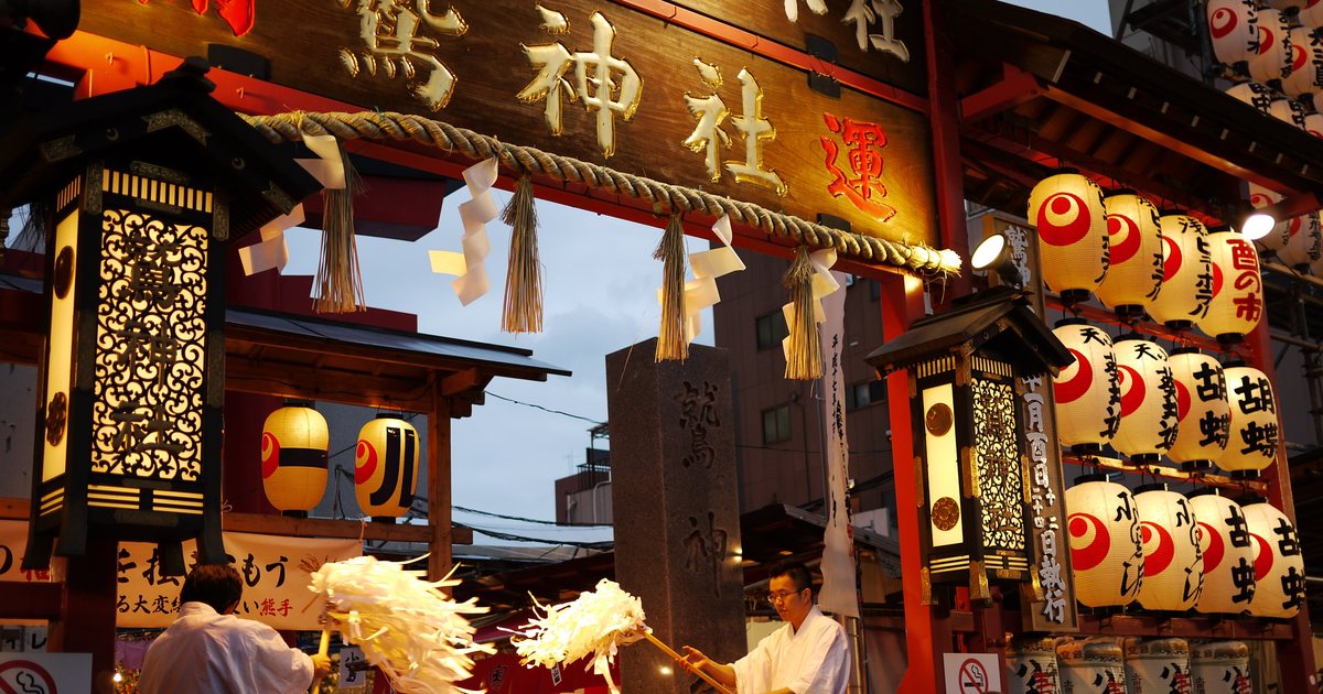 浅草鷲神社的酉の市:社號額下掛著成排寫有「酉の市」的提燈,神職在鳥居前揮舞大幣