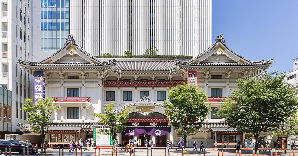 晴天下的歌舞伎座正面全景:左右兩座白色千鳥破風山牆、中央入口上方的唐破風屋簷,屋簷下掛著一整排紅色提燈,入口垂著印有鳳凰丸座紋的紫色暖簾,背後是歌舞伎座塔