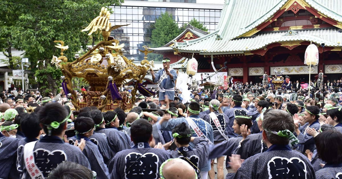神田祭神輿宮入：一基金色神輿被抬進神田明神境內，抬轎者身穿藍染半纏、頭綁綠白手拭，背景是御社殿的銅綠屋頂與朱紅金彩