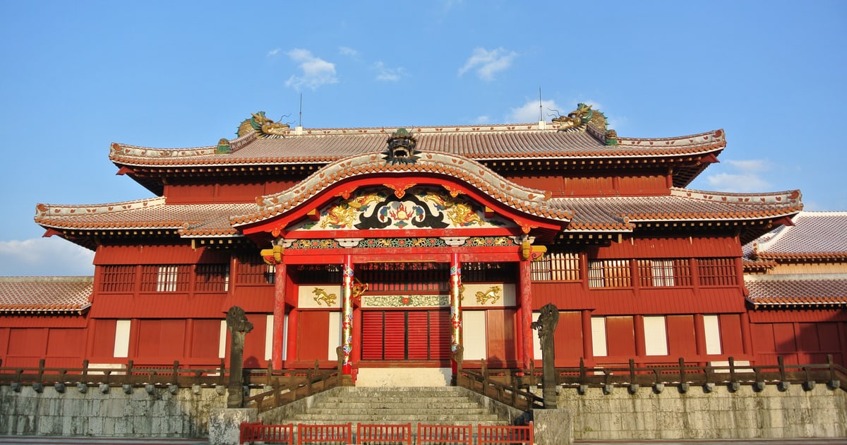 首里城正殿正面:朱漆的重簷木造建築,中央唐破風下方是金色龍與牡丹的彩繪雕刻,屋脊兩端各有一隻綠色龍頭,正面石階兩側各立一根灰色石雕大龍柱,建築下方是珊瑚石灰岩砌成的基壇(2015 年 2 月攝,為 2019 年燒毀的平成復元正殿)