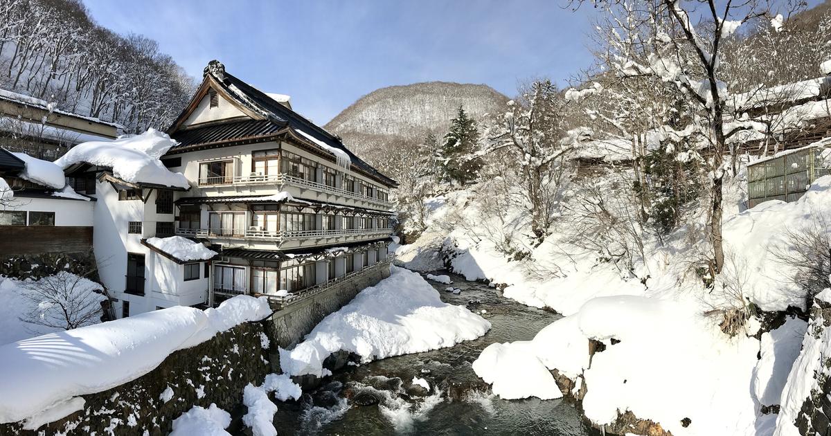 寶川溫泉汪泉閣的冬天:晴天的積雪溪谷裡,多層的和風旅館建物沿著寶川的石砌河岸蓋起,屋頂與兩岸堆滿厚雪