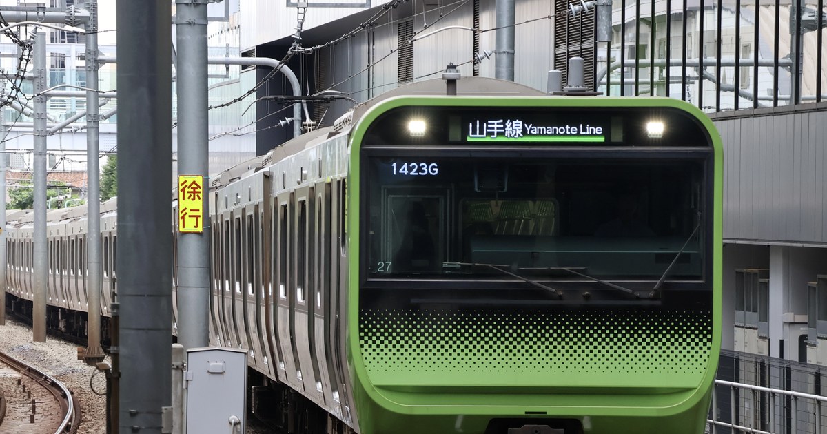 山手線的黃綠色車頭正駛近,前面窗上方的黑底看板寫著「山手線 Yamanote Line」,擋風玻璃上緣顯示運行番號 1423G,左側電線桿掛著紅字黃底的「徐行」牌