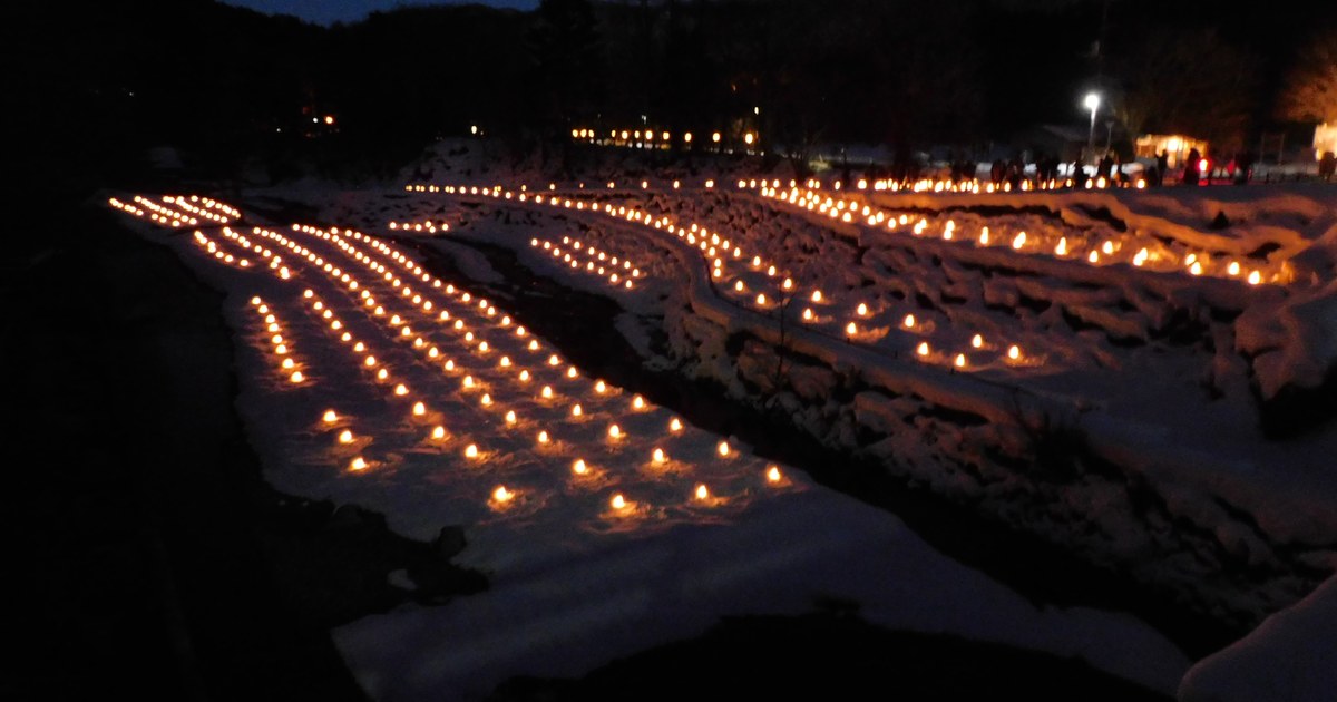 湯西川溫泉かまくら祭的沢口河原入夜,階梯狀的雪地河灘上一排排點著燭光的小雪屋,背後是暗下來的山