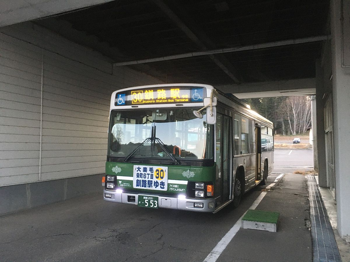 一輛綠白色塗裝的阿寒巴士停在阿寒湖巴士中心的候車雨棚下,車頂電子字幕打著黃色的「30 釧路駅ゆき Kushiro Station Bus Terminal」,保險桿上的牌子寫著「大楽毛・栄町6丁目 30 釧路駅ゆき」,車門開著、車上沒有人