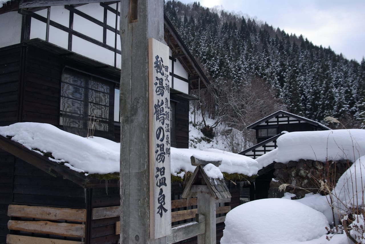 乳頭溫泉鄉鶴の湯雪中的木造建築與「祕湯 鶴の湯溫泉」立牌