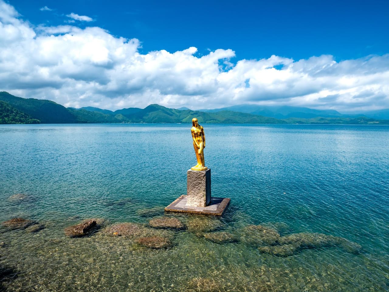 田澤湖畔金色辰子像佇立在清澈見底的湖水中,背景為環湖群山
