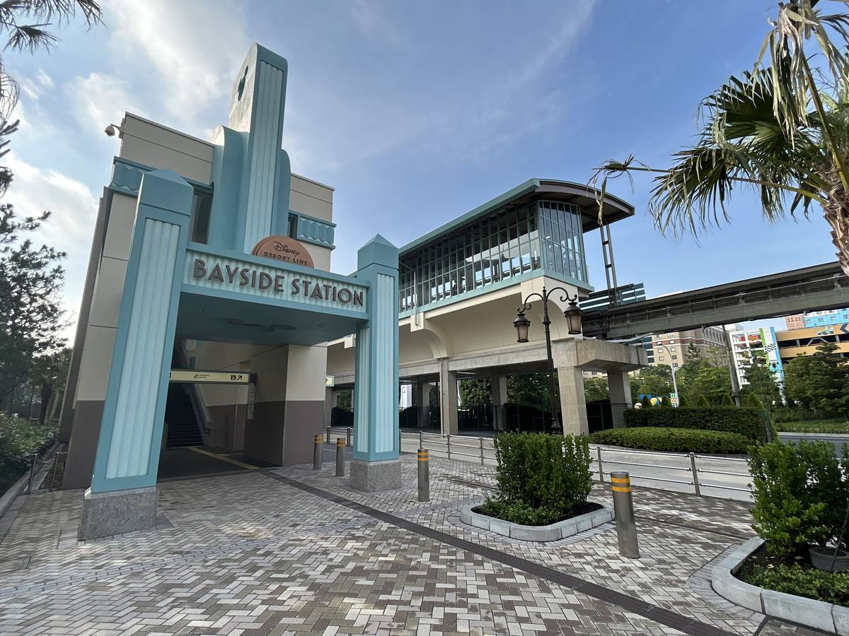 迪士尼度假區線ベイサイド站的站舍入口,淺綠色門框上寫 BAYSIDE STATION,右側是玻璃月台棟與往外延伸的高架軌道