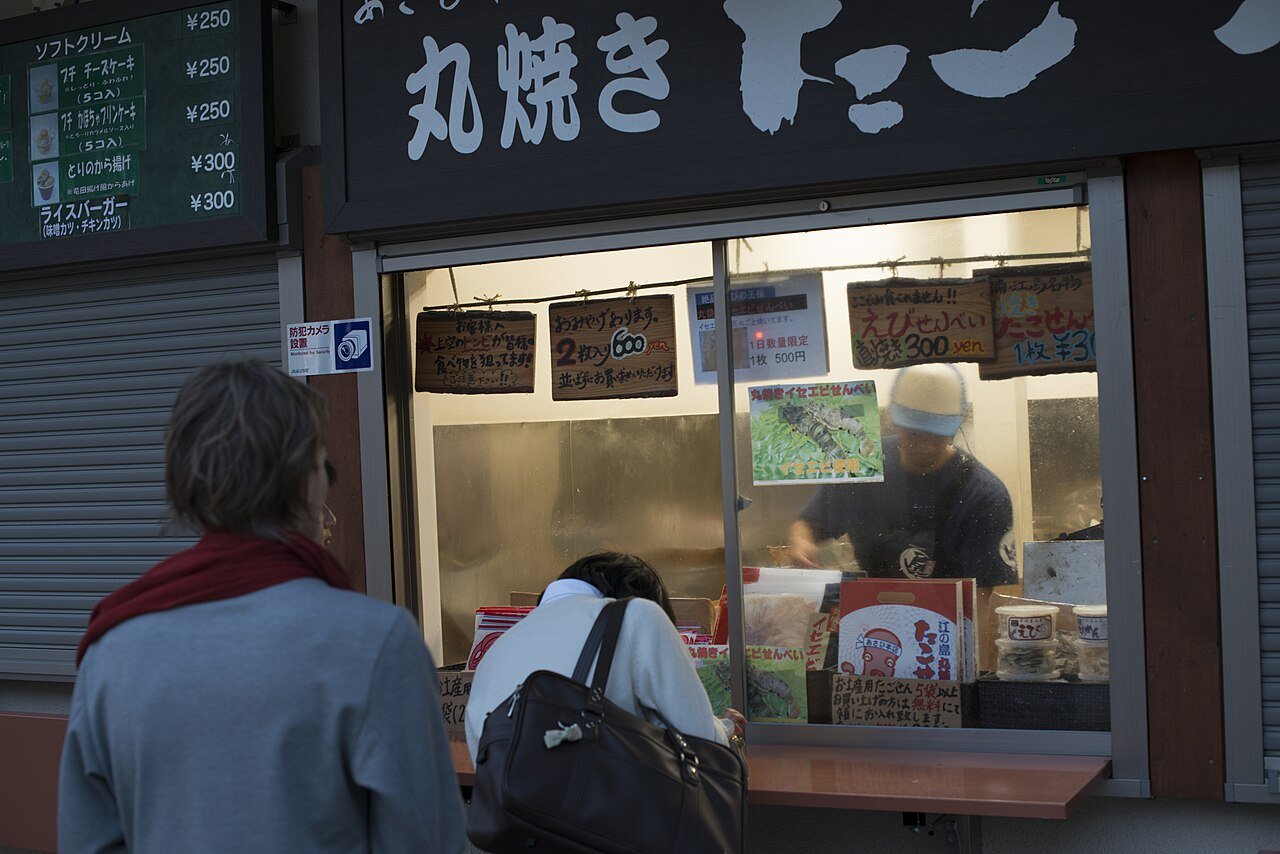 あさひ本店的窗口,職人正在鐵板前現壓丸焼きたこせんべい,遊客在窗外圍觀