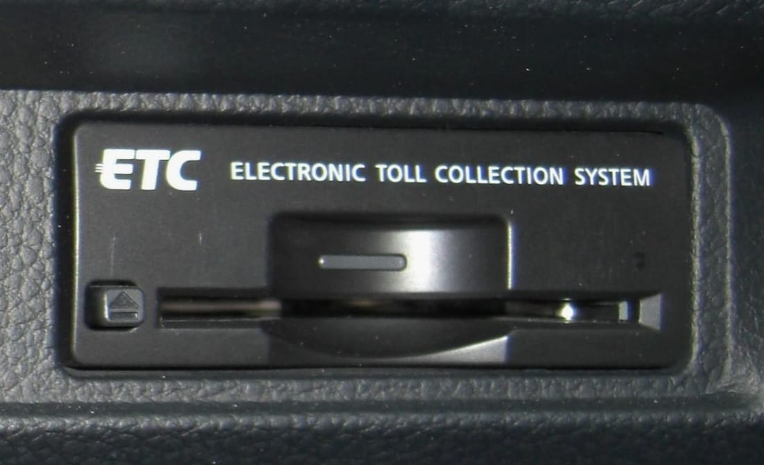 日本車內的 ETC 車載器特寫,機身印有 ETC 與 ELECTRONIC TOLL COLLECTION SYSTEM 字樣,中央為卡片插槽、左側為退卡鍵