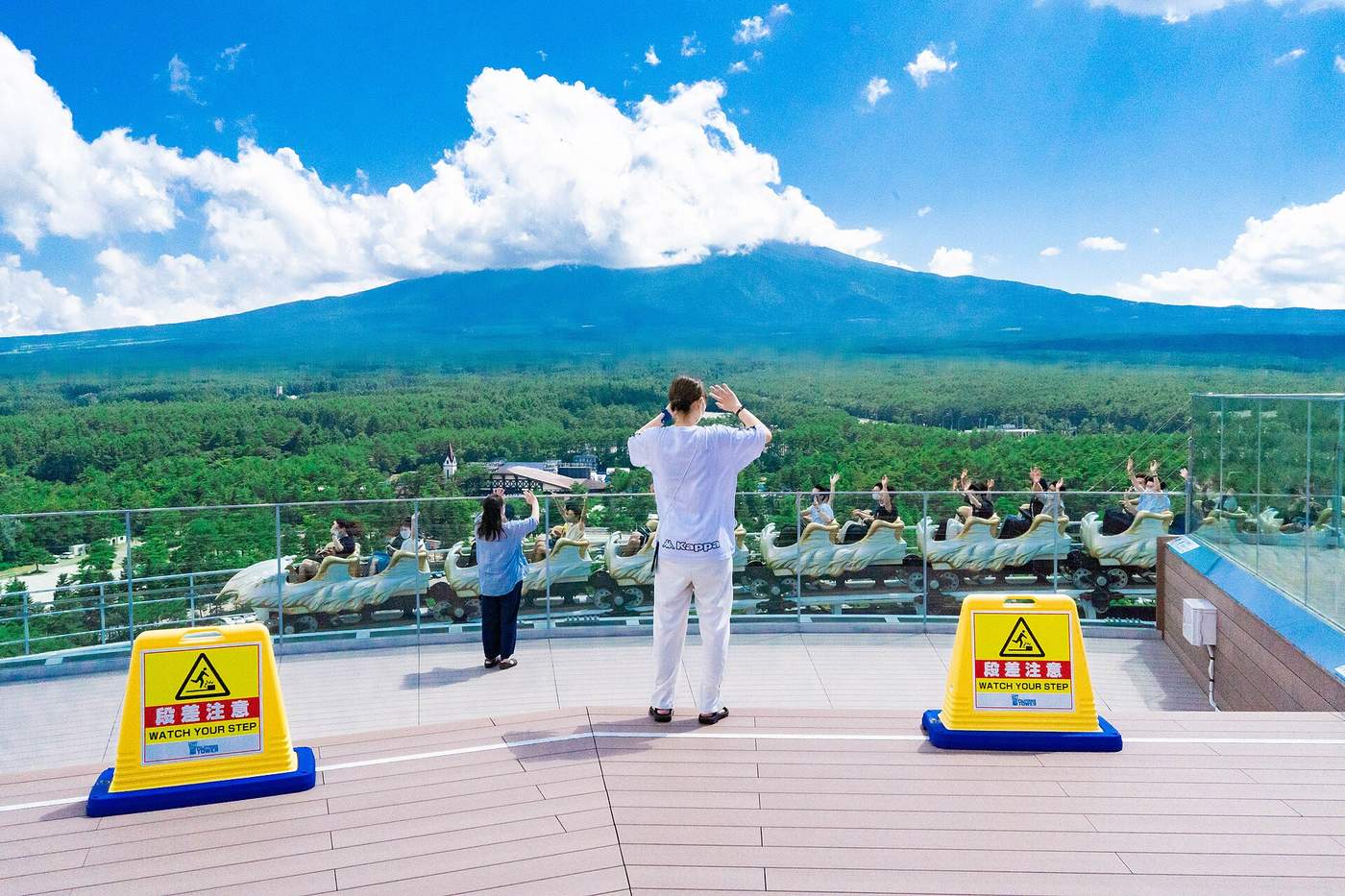 從 FUJIYAMA タワー展望甲板看 FUJIYAMA 過山車列車呼嘯而過,乘客舉手,背景樹海延伸到富士山山腳