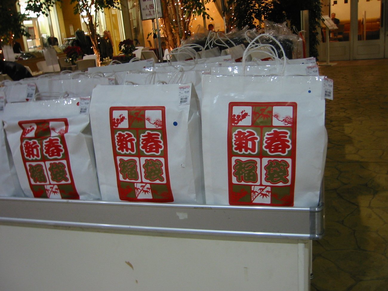 店頭平台上排滿印著「新春福袋」紅綠圖案的白色紙袋，每袋貼著價格標