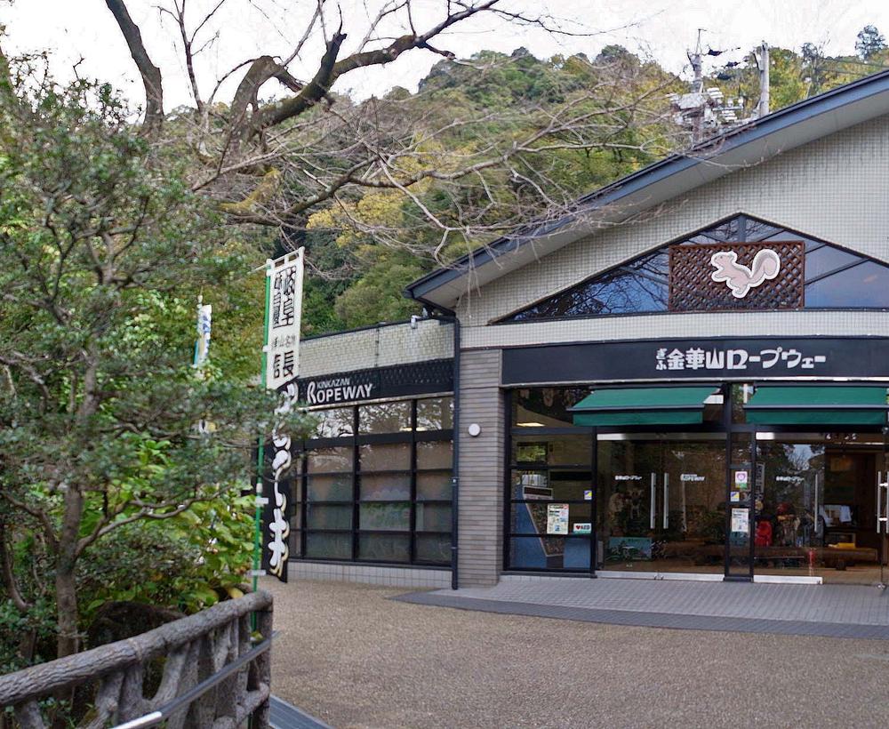 岐阜公園裡的金華山纜車山麓站:灰白色建築正面掛著黑底白字的「ぎふ金華山ロープウェー」招牌,三角形山牆上有松鼠圖案,左邊另一塊招牌寫 KINKAZAN ROPEWAY,入口是玻璃自動門,背後是金華山的樹林