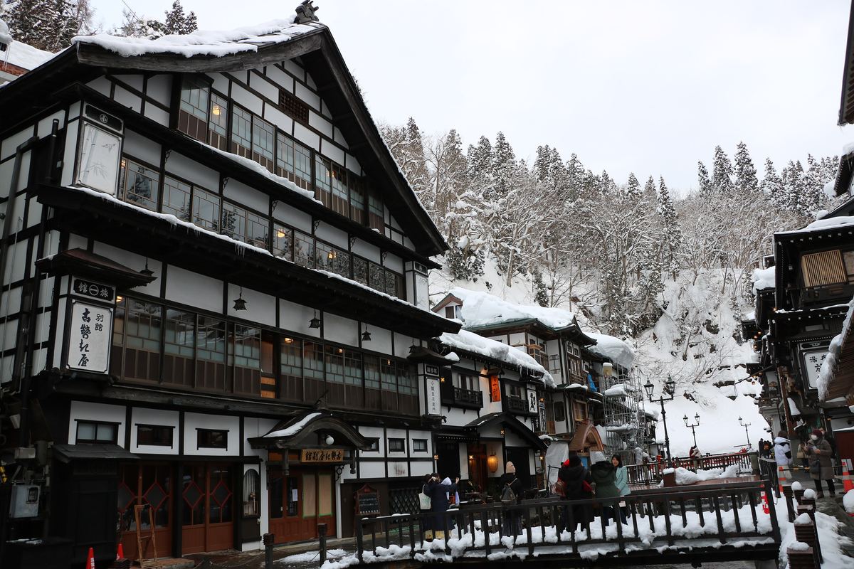 銀山溫泉冬季街景:左側三層木造的古勢起屋別館屋簷積雪垂冰,對岸旅館與覆雪杉林相連