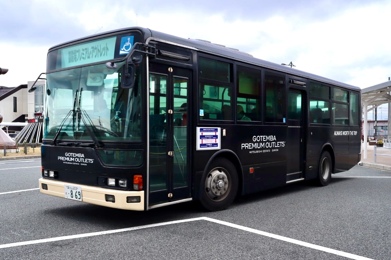 全黑車身的免費接駁巴士停在車站前廣場，車身印有白色 GOTEMBA PREMIUM OUTLETS 與 MITSUBISHI ESTATE·SIMON 字樣，車頭方向幕顯示「御殿場プレミアム・アウトレット」