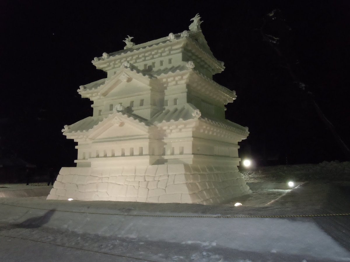 夜裡打燈的巨大雪像,用雪做成三層天守的模型,底下是雪雕的石垣,前方拉著一條繩子隔開觀眾,四周是黑色夜空