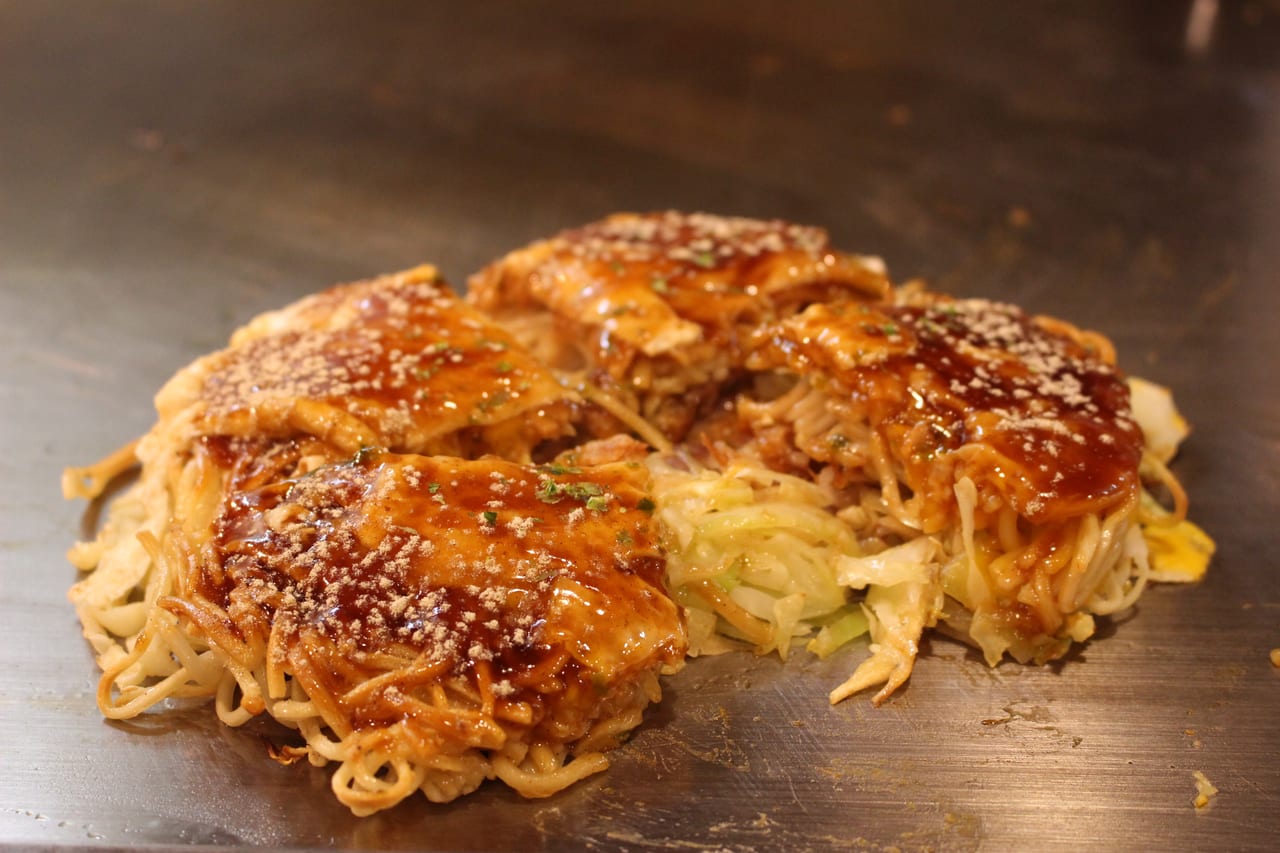 A finished Hiroshima okonomiyaki on the griddle with fried noodles and cabbage