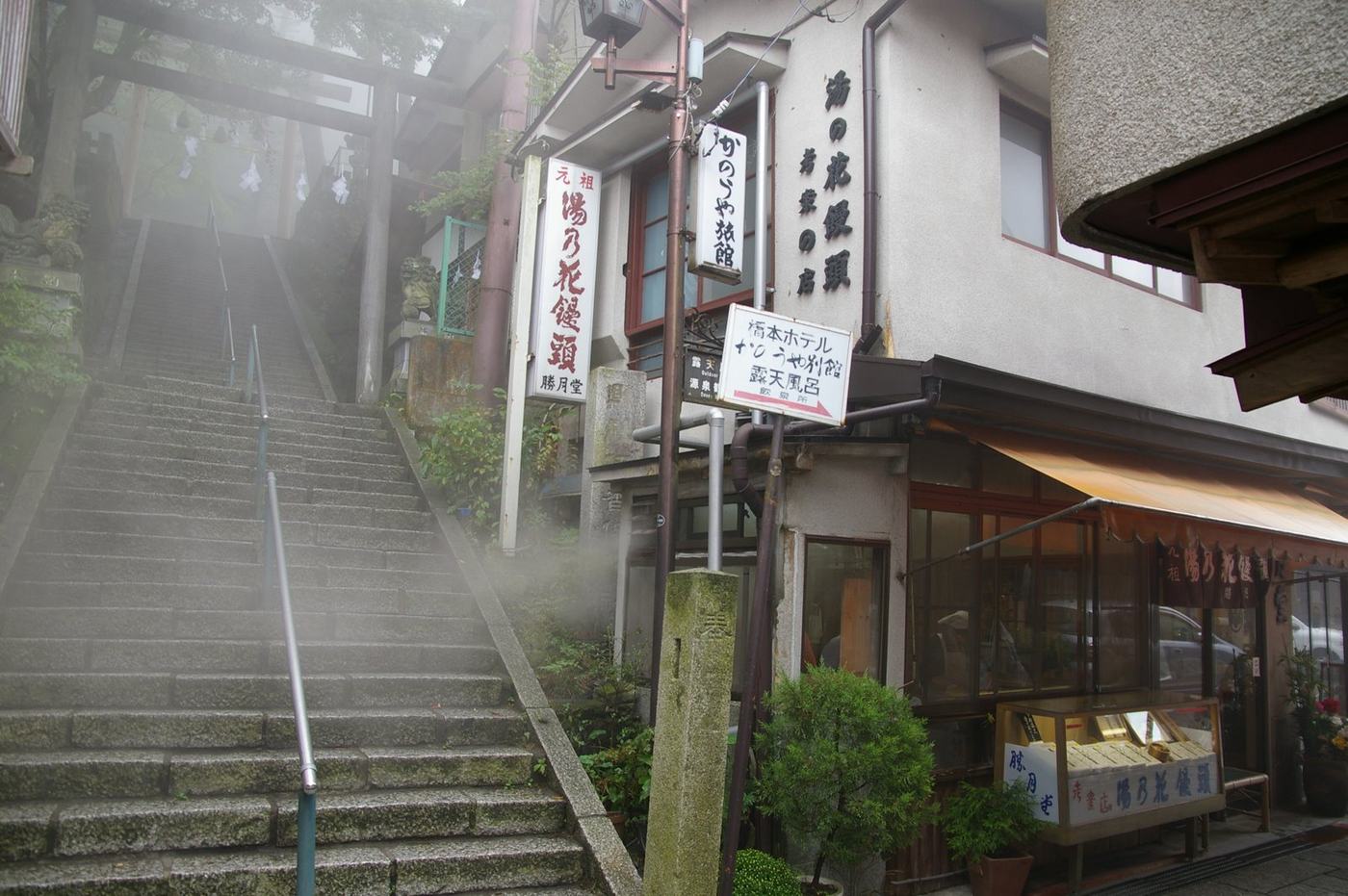 霧氣中的伊香保石段街末段,石階盡頭立著伊香保神社的木造鳥居,右側是掛著湯乃花饅頭招牌的店家