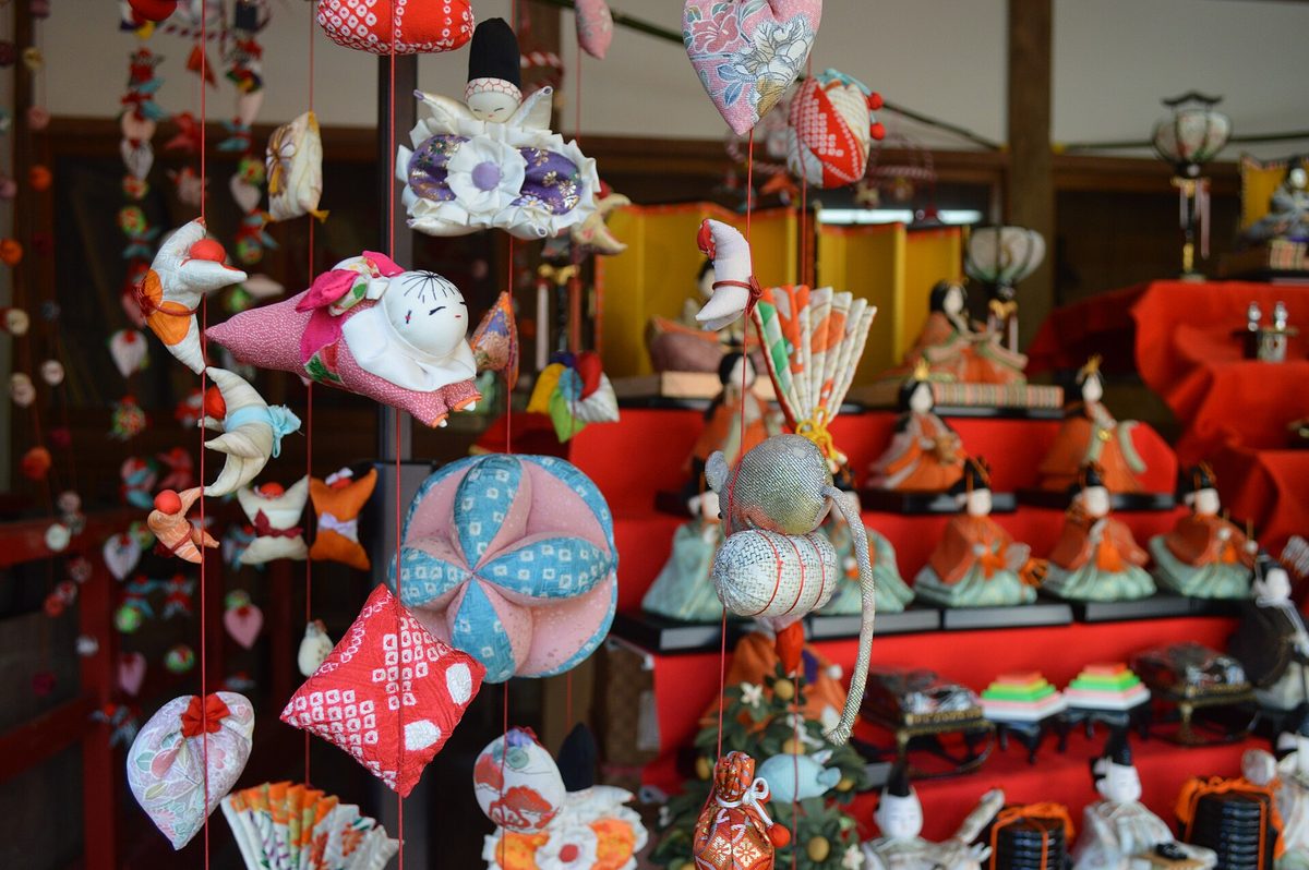 稲取八幡神社裡的雛のつるし飾り:一條條紅線垂吊著手縫的布偶、布球與扇形吊飾,後方是鋪紅毛氈的雛人形階梯