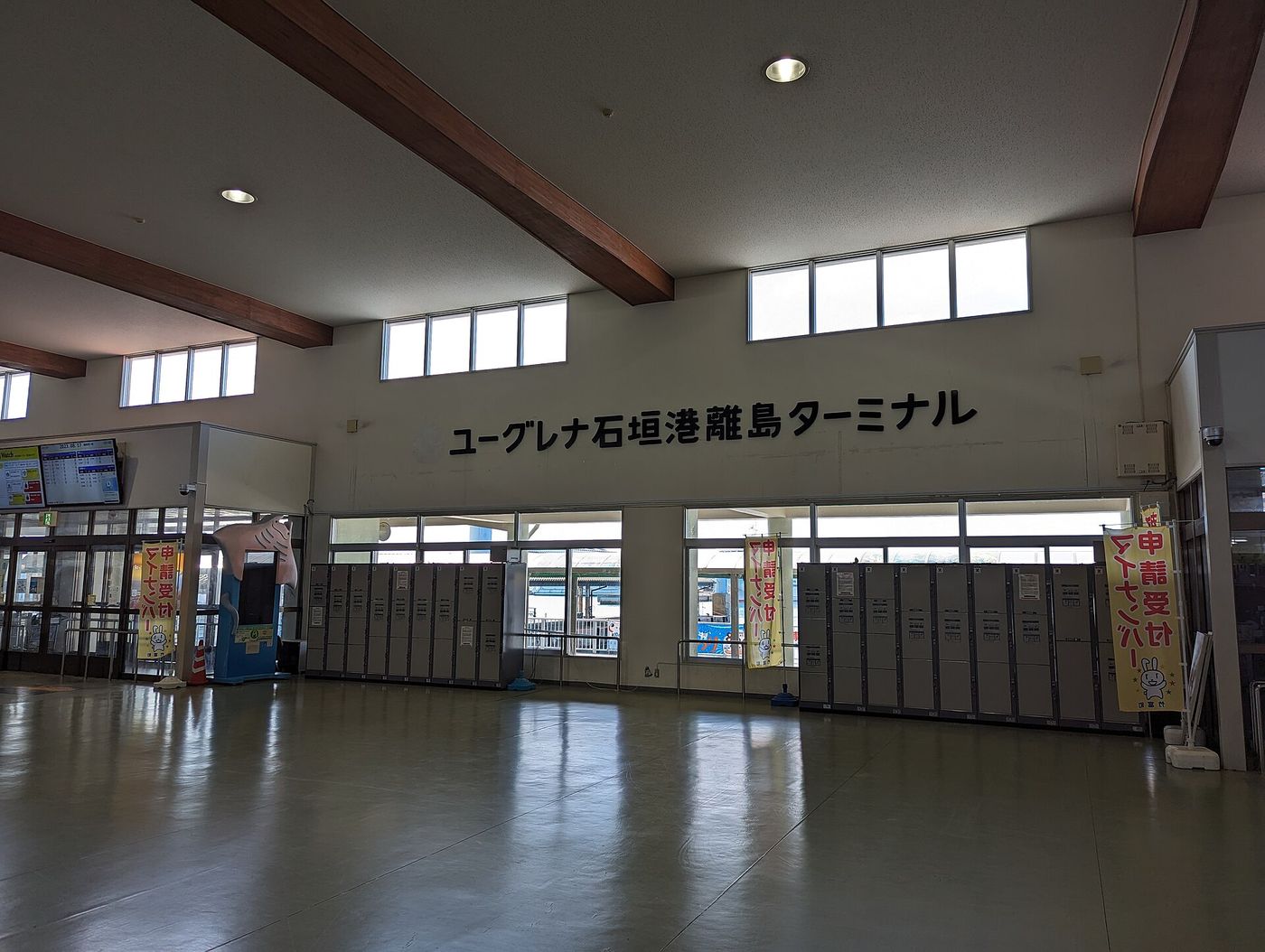 ユーグレナ石垣港離島ターミナル大廳，牆上寫著設施名稱，下方一整排投幣置物櫃，左上角是班次顯示螢幕