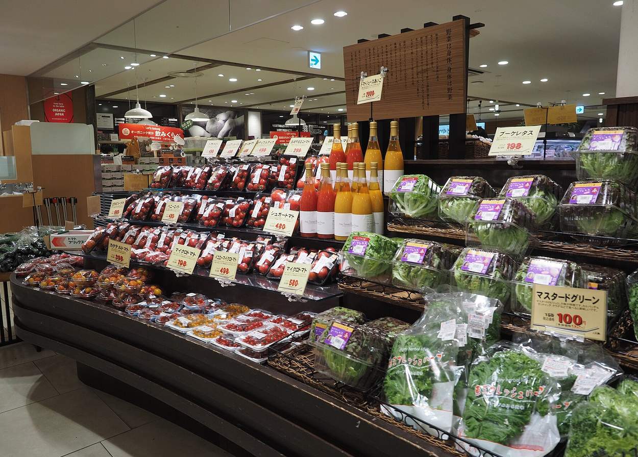 日本超市的生鮮蔬果賣場，番茄、生菜與蔬果汁排開並貼著手寫價格牌