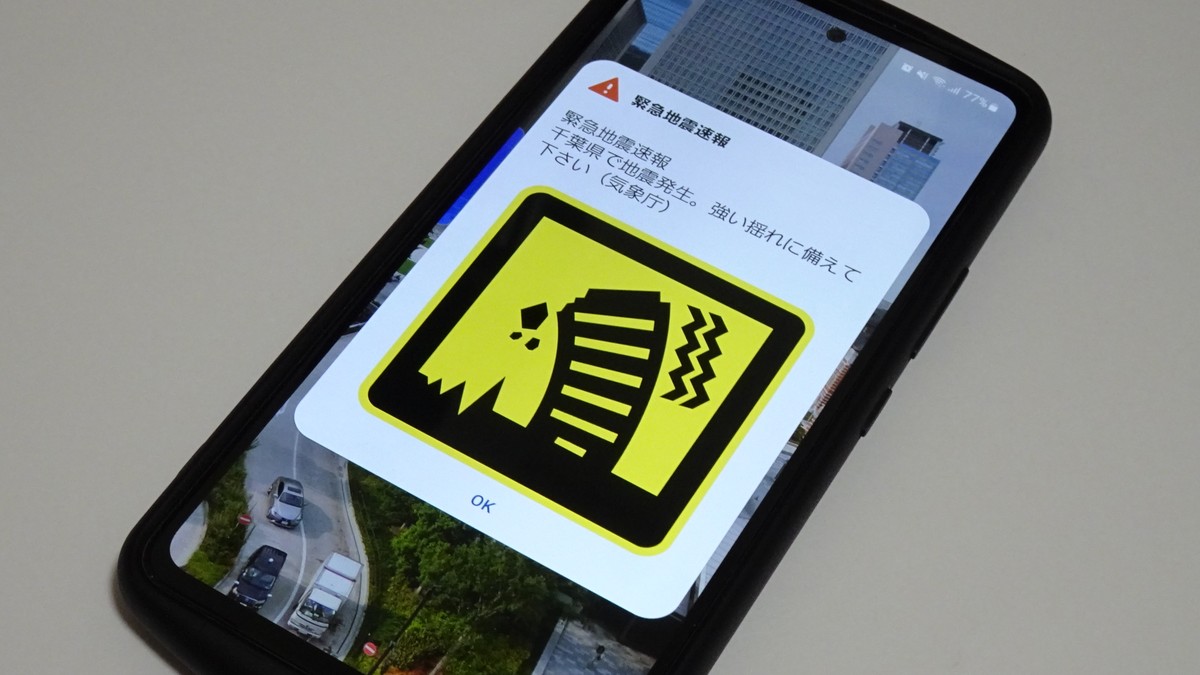 日本手機螢幕上顯示緊急地震速報的黃底警示畫面，上方寫著地震速報字樣與發生地區