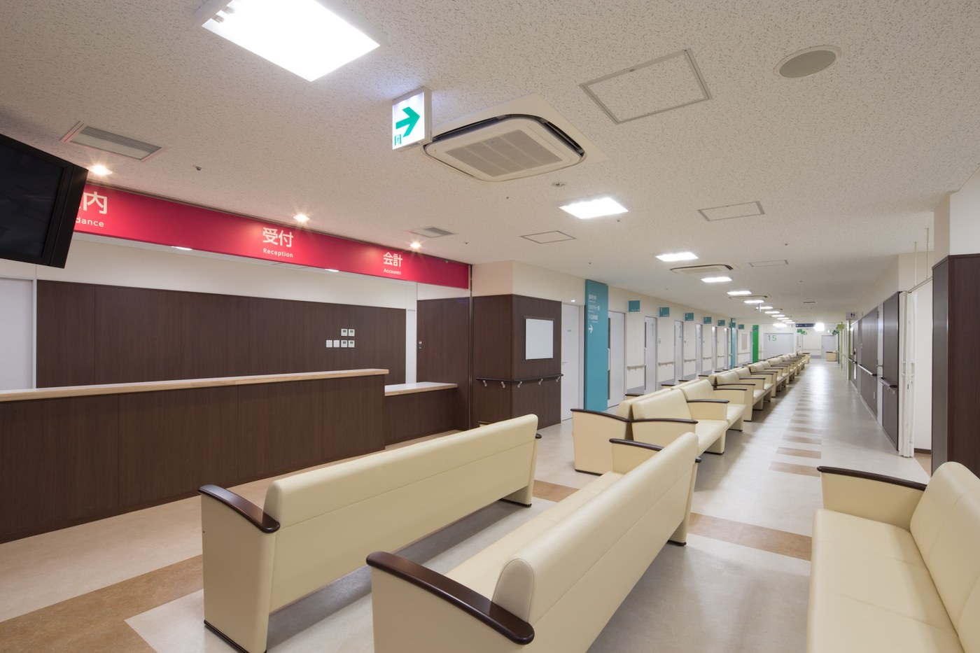 日本醫院外來大廳,深紅色橫幅標示牌由左至右寫著「案内 Guidance」「受付 Reception」「会計 Accounts」,日文下方各附一行英文,下方是深木色櫃檯與成排米色候診長椅,右側走廊延伸出一整排診間門