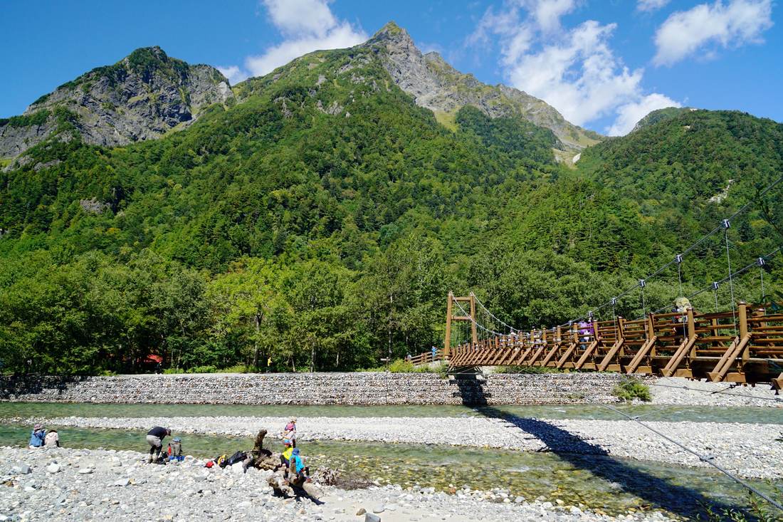 橫跨梓川的明神橋吊橋與背後的明神岳，橋面可見健行者