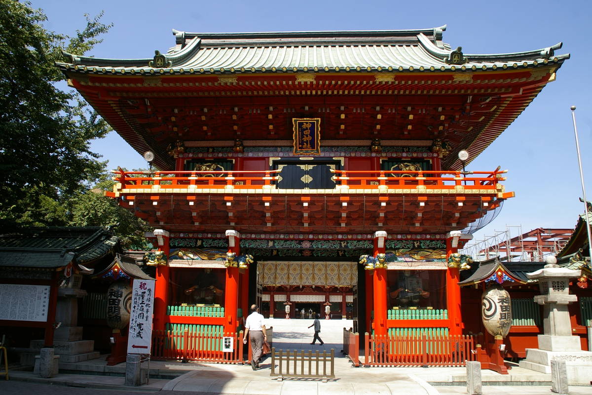 神田明神隨神門：朱紅色雙層樓門配綠色銅瓦屋頂，屋簷下懸藍底金字「神田神社」匾額，左右各掛一只寫著「神田明神」的白色大提燈，門洞內可見遠處的御社殿