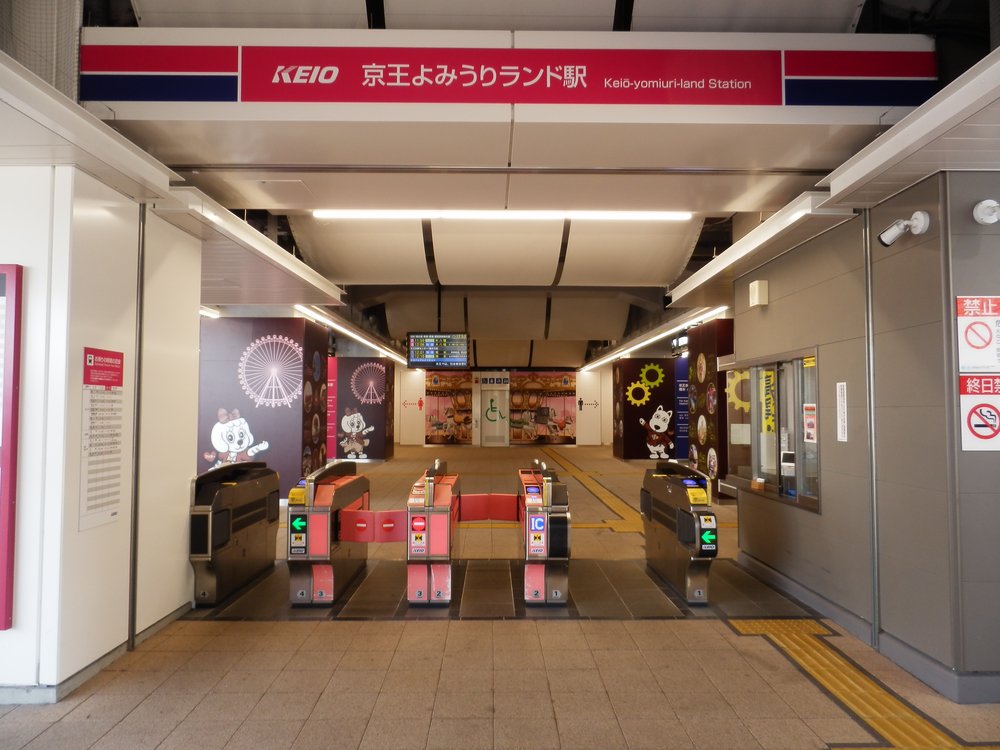 京王よみうりランド駅的剪票口:上方紅色站名招牌,一排自動驗票閘門,閘門後的牆上畫著摩天輪與讀賣樂園的狗吉祥物