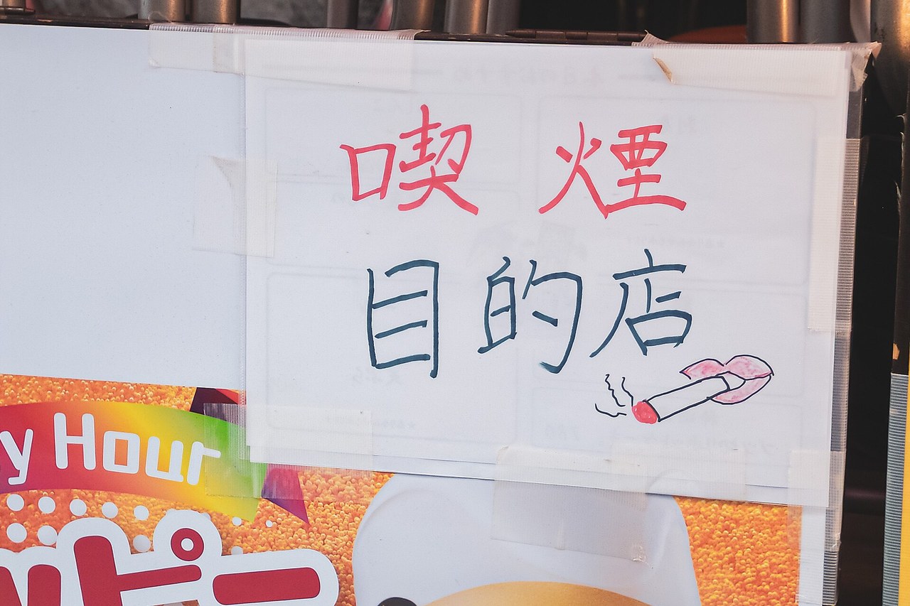 神田一家店門口貼的手寫告示,紅字寫喫煙、黑字寫目的店,旁邊畫著一根點燃的香菸