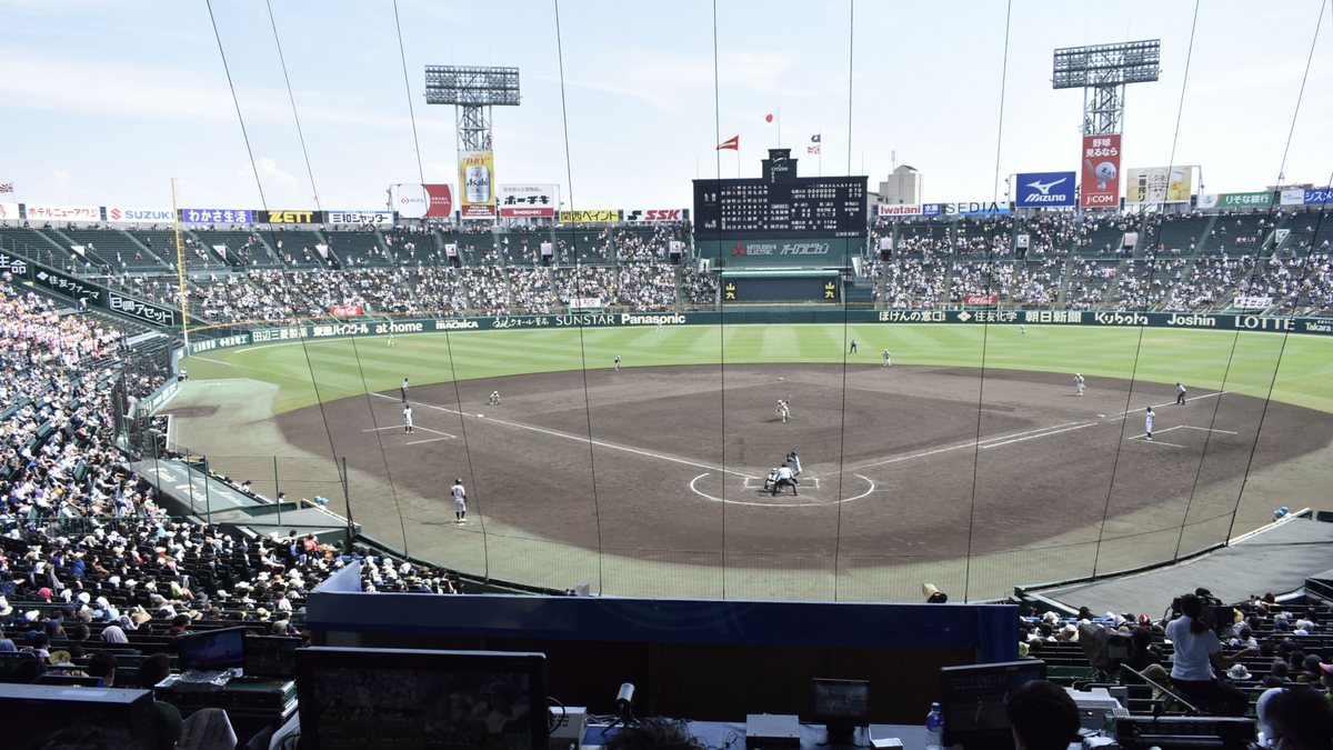 夏季甲子園高校野球的比賽畫面:白色制服的高中球員在場上,看台坐滿觀眾,記分板顯示比賽進行中