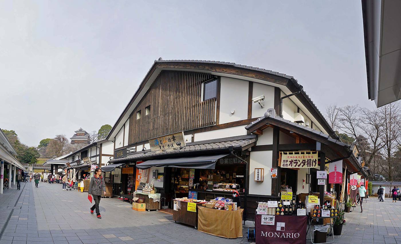 熊本城城彩苑的桜の小路商店街,木造店鋪掛著甘酒與オランダ揚げ的招牌,街底遠處是天守閣