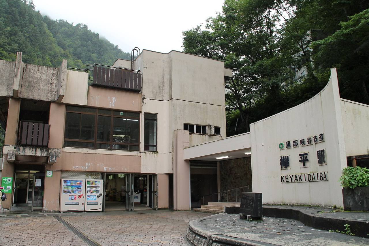 欅平站站舍全景,右側弧形白牆刻著站名,左側水泥建築前有自動販賣機與售店入口,中央是往驗票口的有頂通道