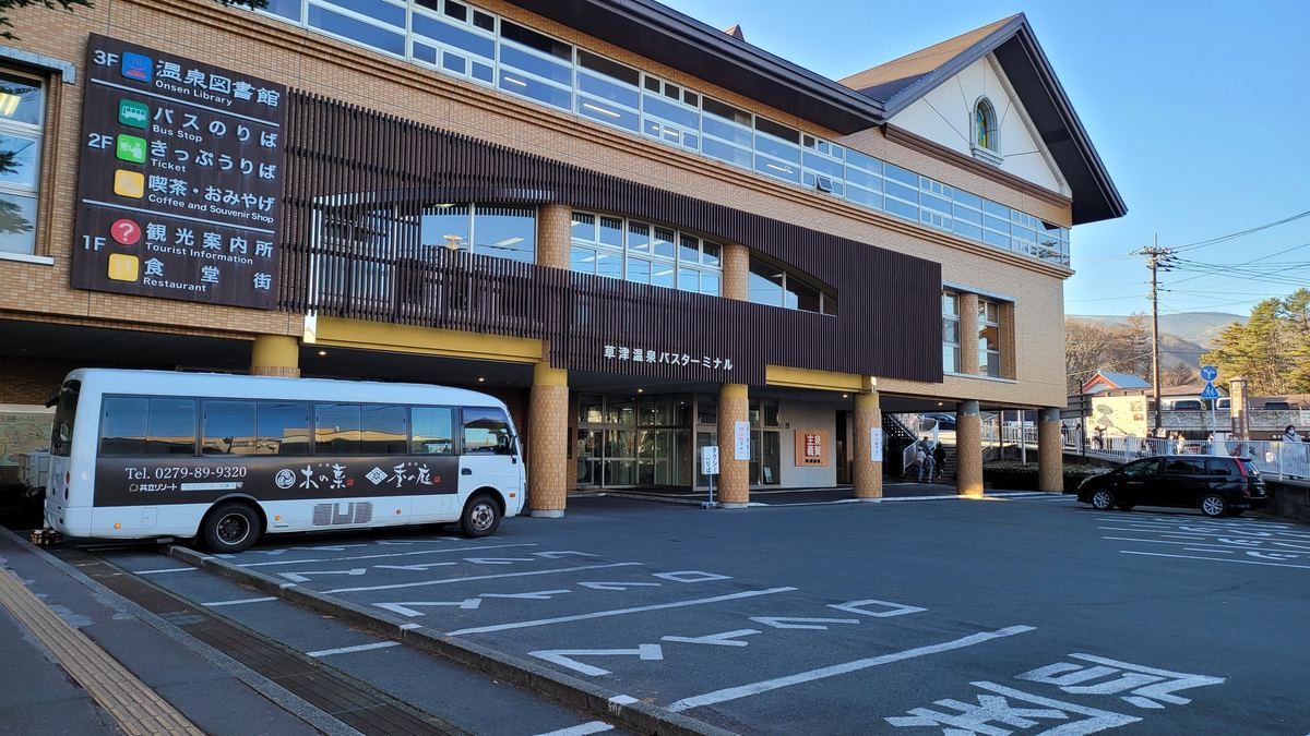草津溫泉巴士總站外觀，牆上樓層看板寫著 3F 溫泉圖書館、2F 巴士乘車處與售票處、1F 觀光案內所與食堂
