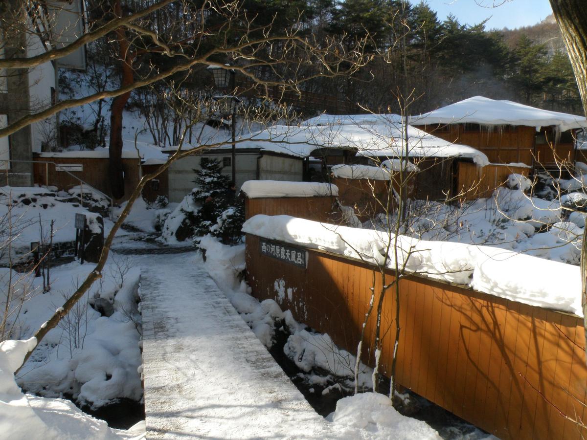 雪中的西の河原露天風呂，木板圍牆上掛著「西の河原露天風呂」名牌，前方是積雪的小橋