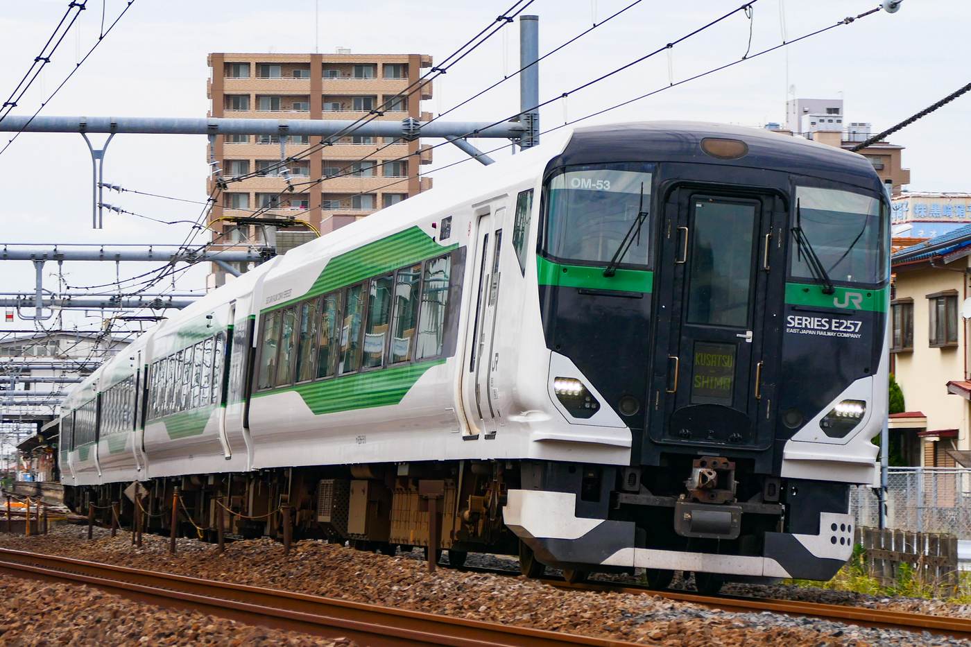 特急「草津・四万」的 E257-5500 系電車：白色車身配綠色腰帶，車頭下方的方向幕顯示 KUSATSU SHIMA，車輛正沿著架空電線下的彎道行駛