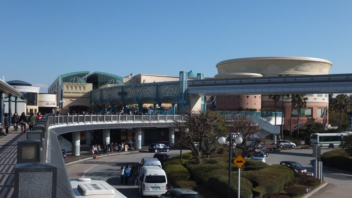 從舞浜站南側的天橋往前看:正中間米色建築寫著 RESORT GATEWAY STATION,最左邊的圓形小樓是東京迪士尼度假區歡迎中心,右邊藍綠色拱廊是 Ikspiari,高架軌道從右側橫過