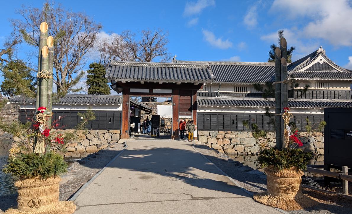 松本城黑門二之門與跨過內護城河的參道，門洞裡是圍欄圍出的入場動線，兩側立著過年的門松