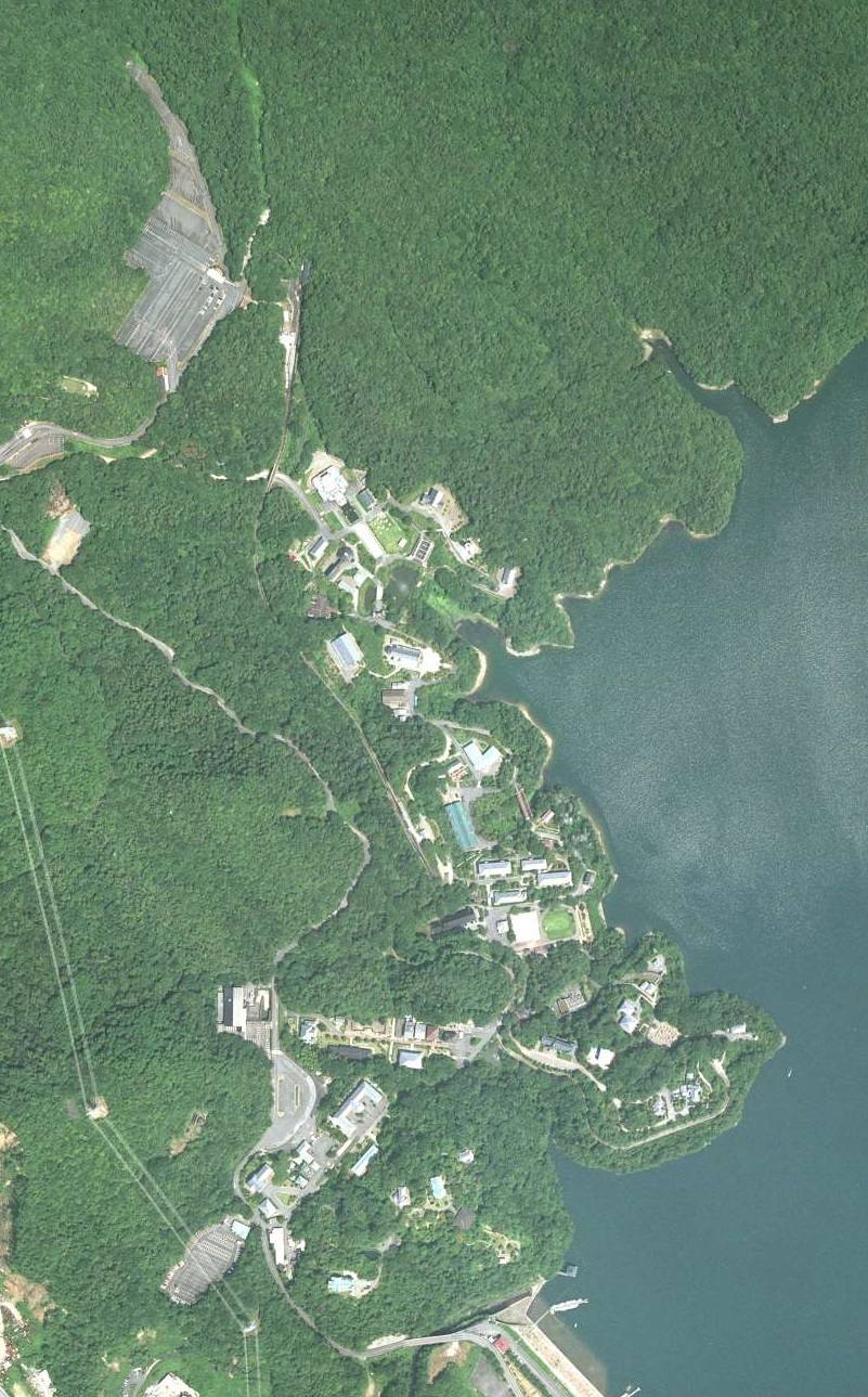 航空照片：明治村的建物沒有集中成街區，而是在深綠色樹林裡沿著一片大水域的岸線拉成細長一條