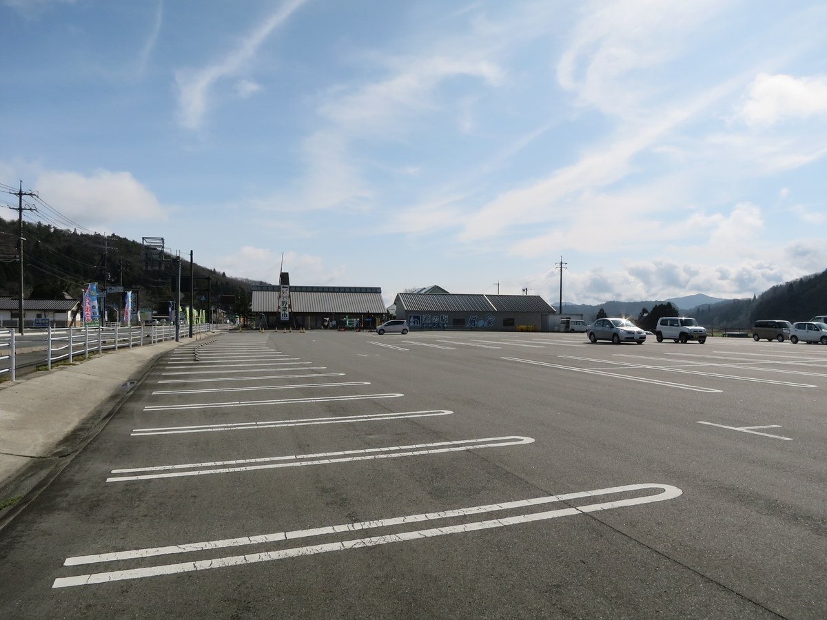 道の駅風の家的西側停車場,白線劃出的一大片普通車車格幾乎全空,只有最靠近站舍的那一排停著十來輛車,遠處是金屬屋頂的站舍與山稜。