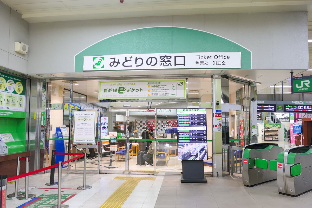 JR 東日本福島站的みどりの窓口門面,綠色拱形招牌下標著 Ticket Office、售票处,左側公告欄貼著營業時間,店內候位區有一位帶行李箱的旅客