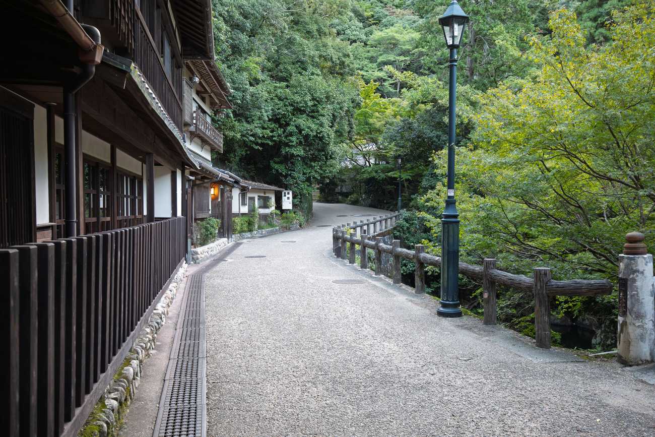 箕面滝道的鋪裝路面,平整步道沿溪谷延伸,左側是木造茶屋、右側是木柵欄與路燈,整段沒有階梯