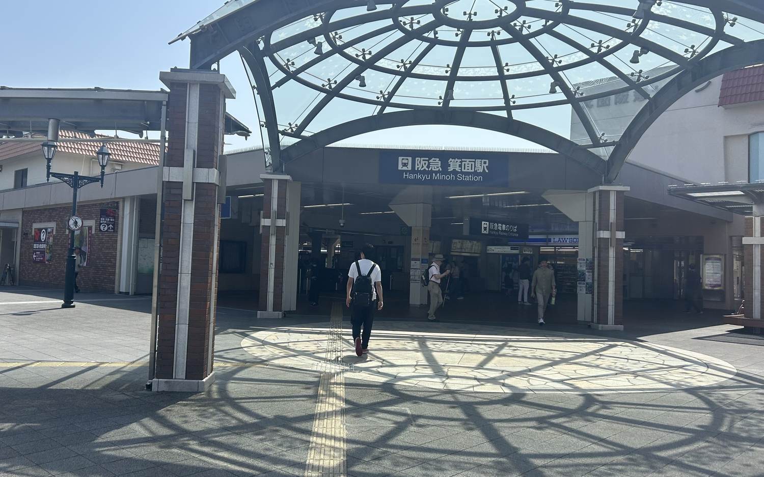 阪急箕面駅站前廣場,拱形玻璃雨棚下掛著藍底白字的「阪急 箕面駅 Hankyu Minoh Station」站名招牌,右側是便利商店與「阪急電車のりば」指標