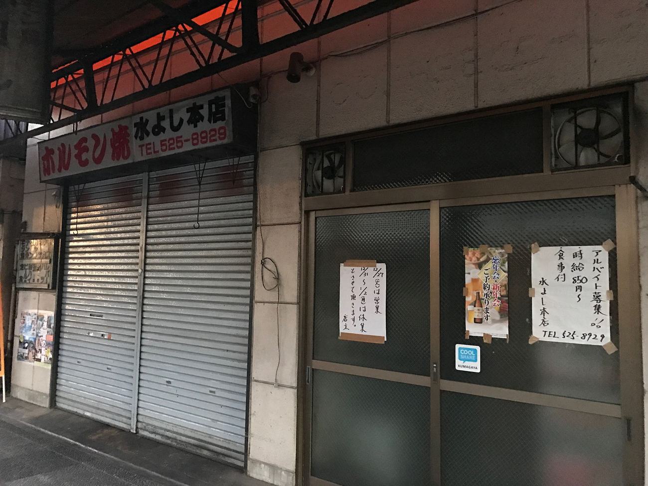 日本個人店家拉下的鐵捲門與門上手寫的年末年始休業告示，寫明哪幾天休業、哪天再開