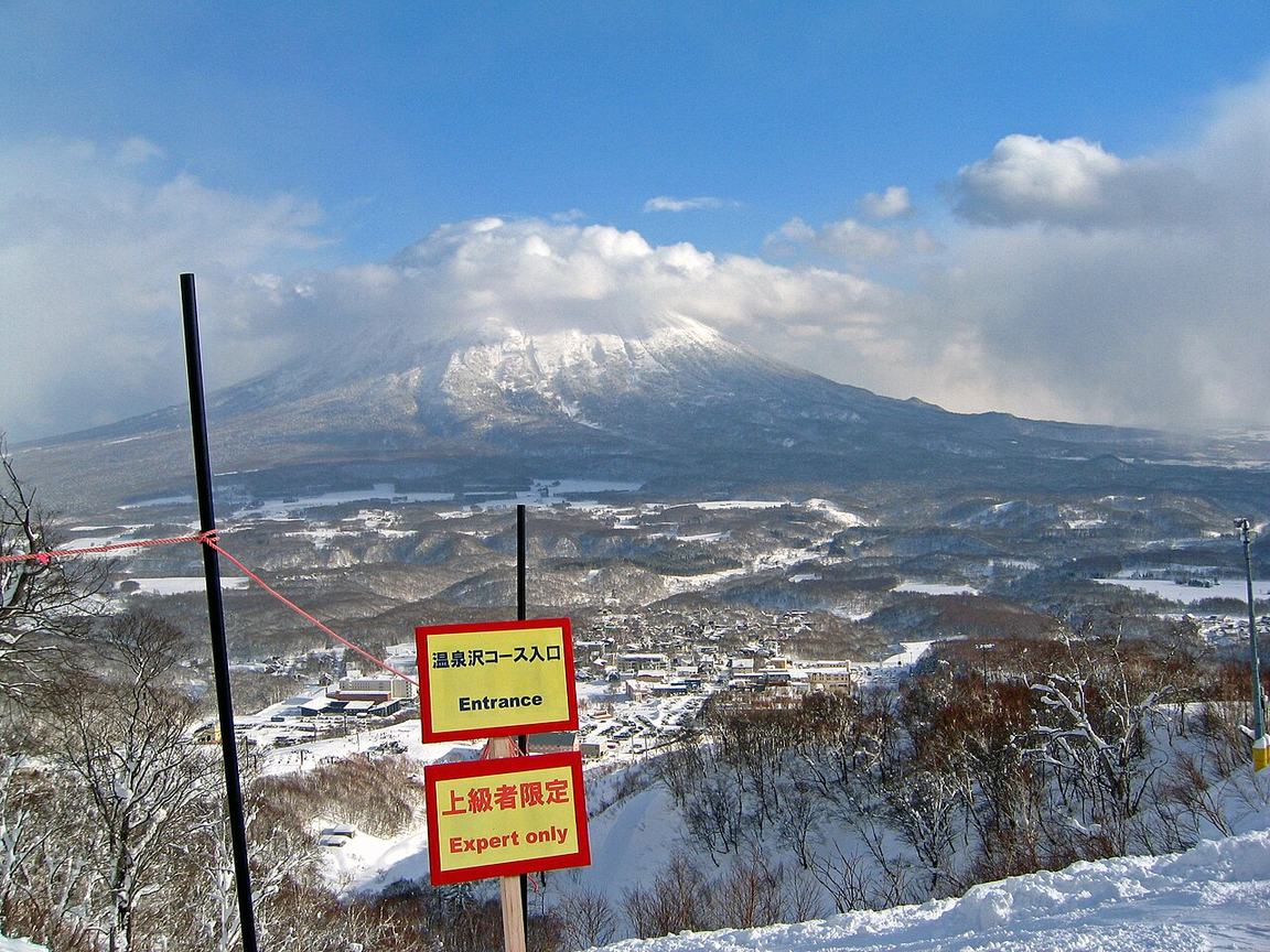 二世谷グラン・ヒラフ雪場的紅色境界繩與雙語告示牌「温泉沢コース入口 Entrance/上級者限定 Expert only」,背景是雲罩頂的羊蹄山