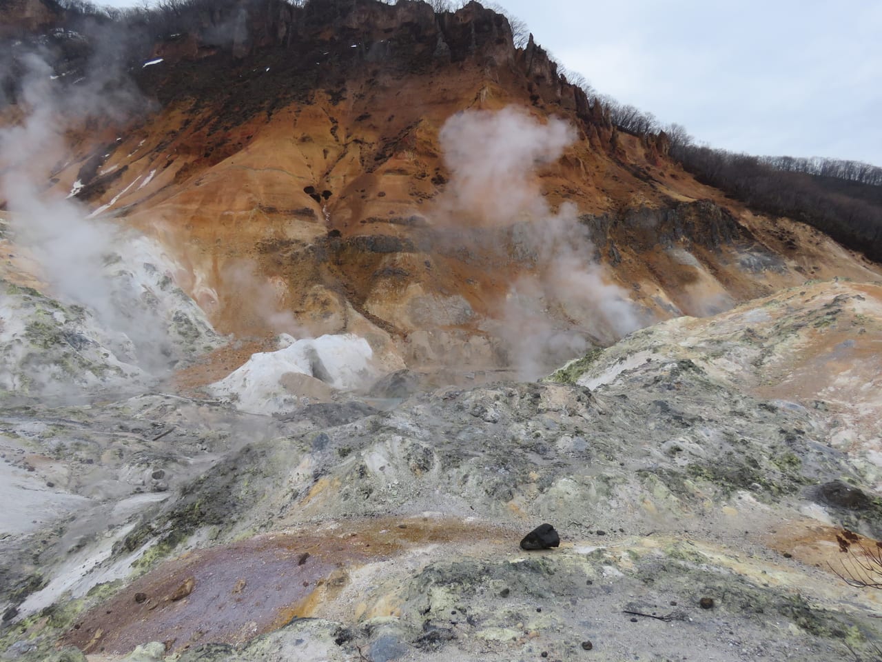 登別地獄谷的火山噴發地形,灰白色岩面與硫磺白煙、鋪設木棧步道
