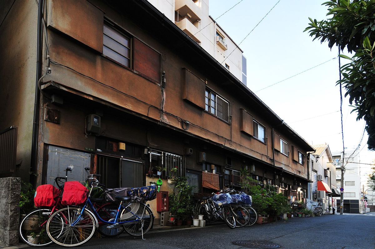 大阪天満橋一帶的住宅巷弄,一整排兩層樓的老式文化住宅沿街展開,門前停滿加了雨罩的腳踏車與成排盆栽,後方是新蓋的高層住宅大樓