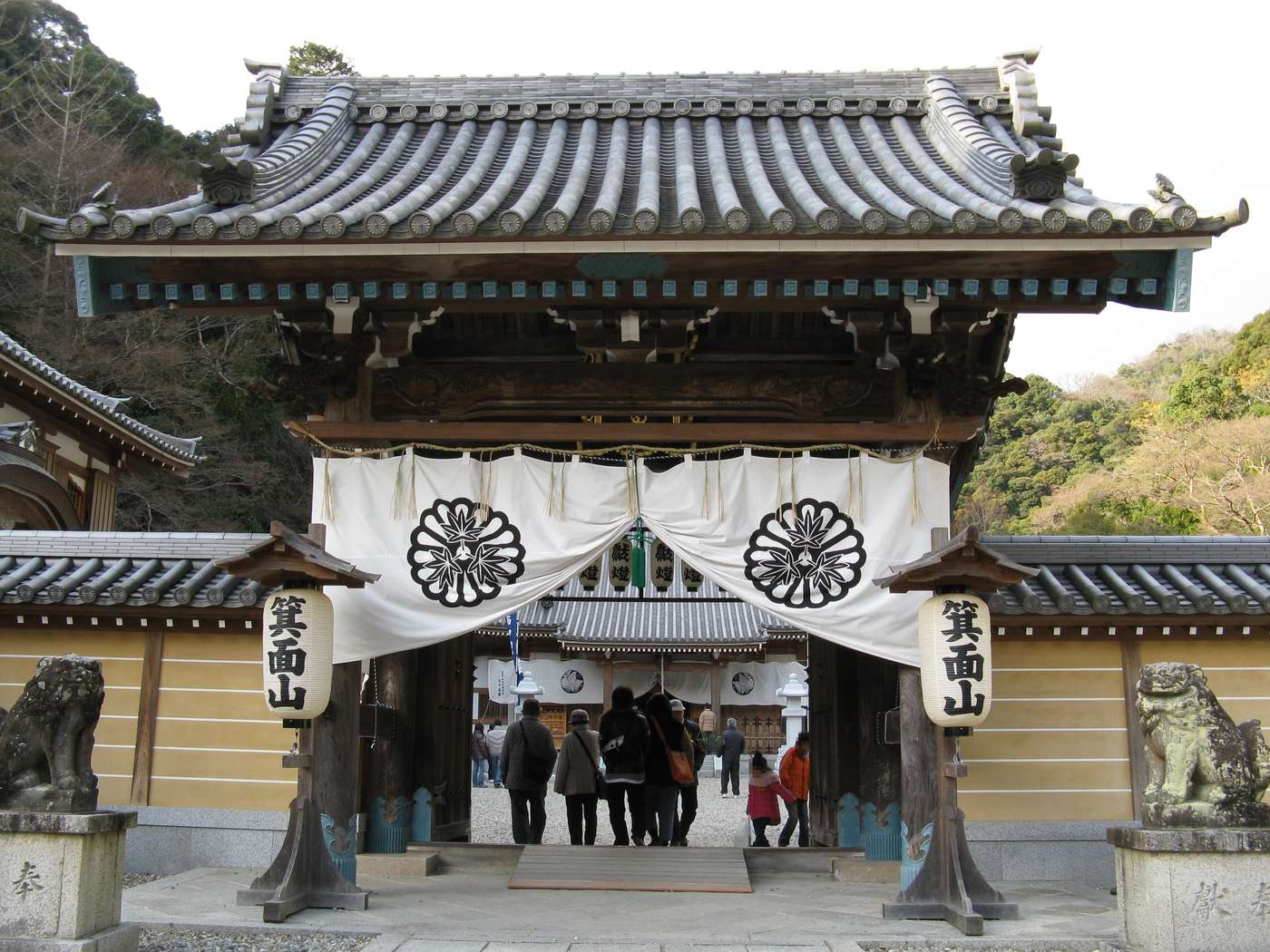 瀧安寺山門,白色暖簾印著寺紋,兩側掛著寫有「箕面山」的大燈籠,門前左右各一尊石造狛犬